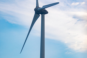 Close-up of a sleek wind turbine with rotating blades set against a bright blue, a Technology Photo by Ales Munt