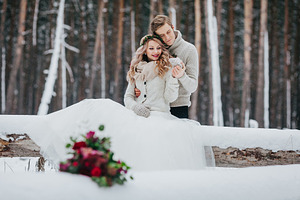 Bride and groom are sitting on the log in the winter forest. Close-up. Winter wedding. Soft focus on the couple
