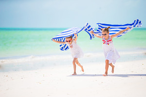 Little girls having fun running with towels on tropical beach containing