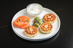 Savory Syrniki with Smoked Salmon, Olives and Sour Cream on White Plate