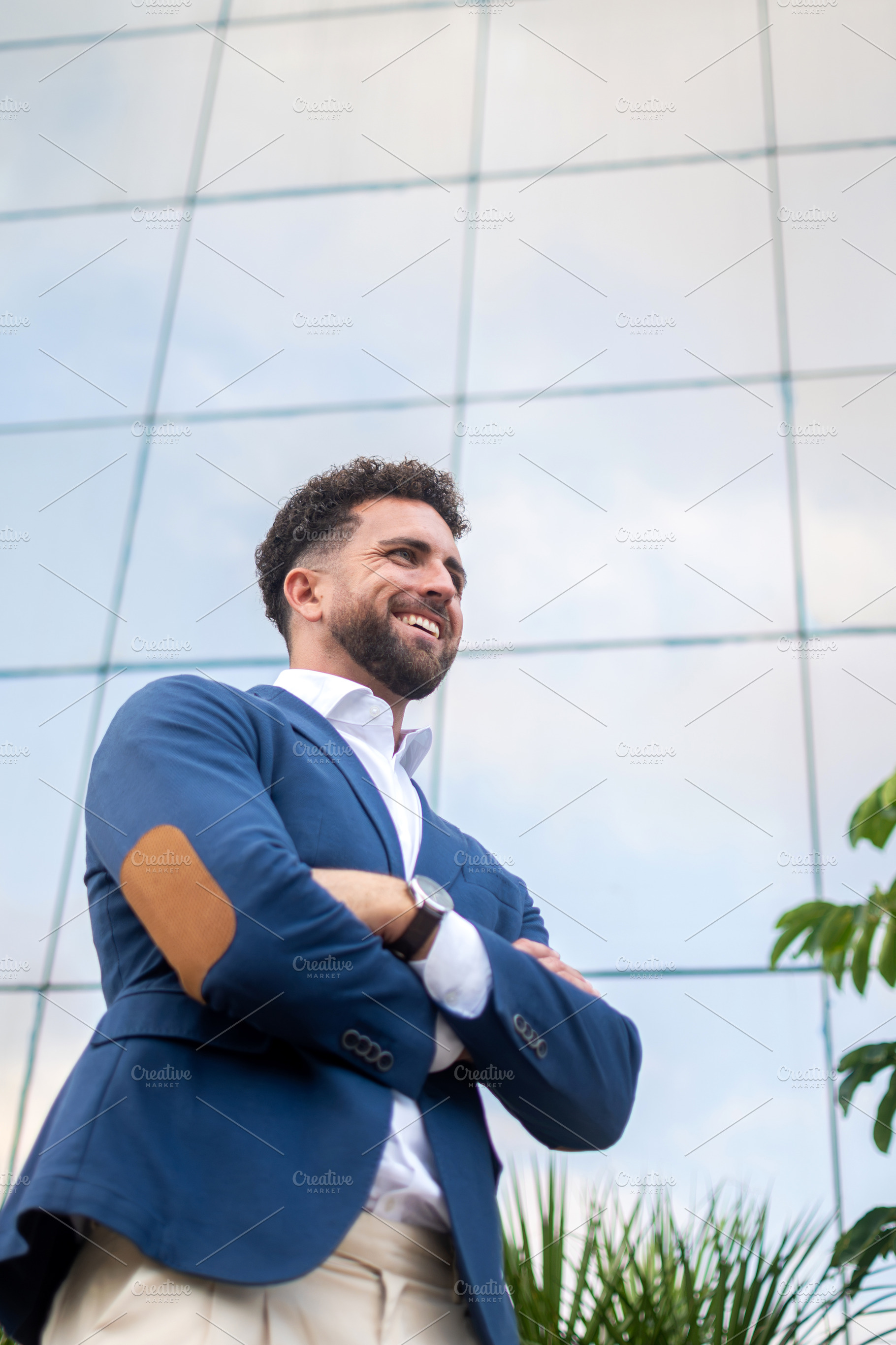 Confident businessman standing with crossed arms outside modern office, a Business Photo by etorres69