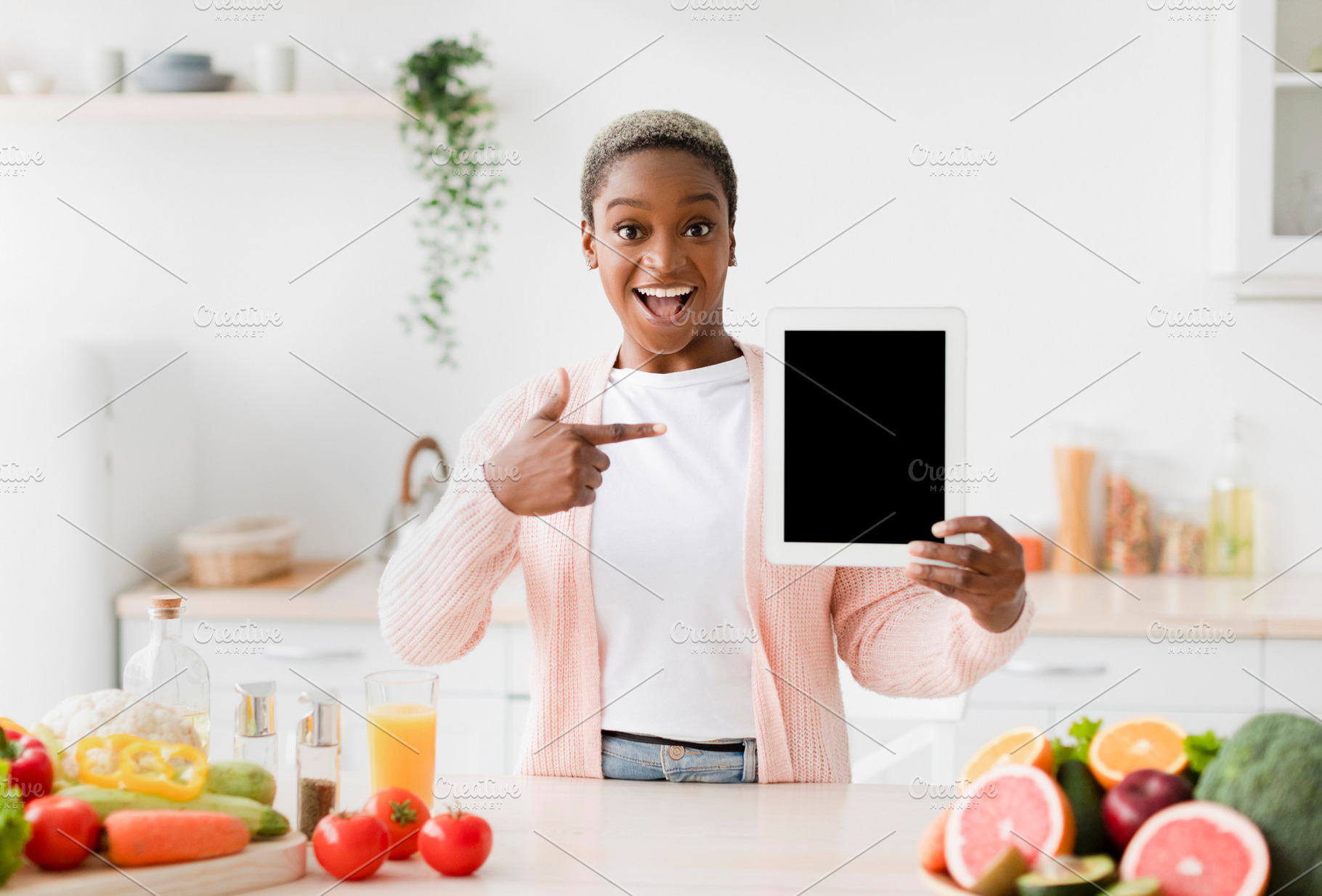 Glad excited emotional young pretty black woman points finger at tablet with bl, a Person Photo by Prostock-Studio