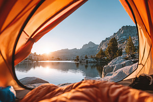 Opening tent door reveals tranquil lake and mountains at sunrise, a Photo by AlyaAnd