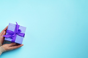 Female hands holding a blue gift box on a blue background, a Holiday Photo by ndanko