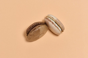 Two brown macarons on beige background, top view, a Food & Drink Photo by ndanko