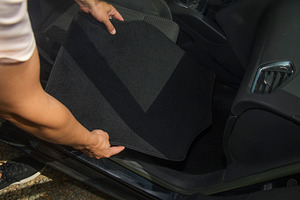 a man places a new mat onto the car floor, a Photo by Nito
