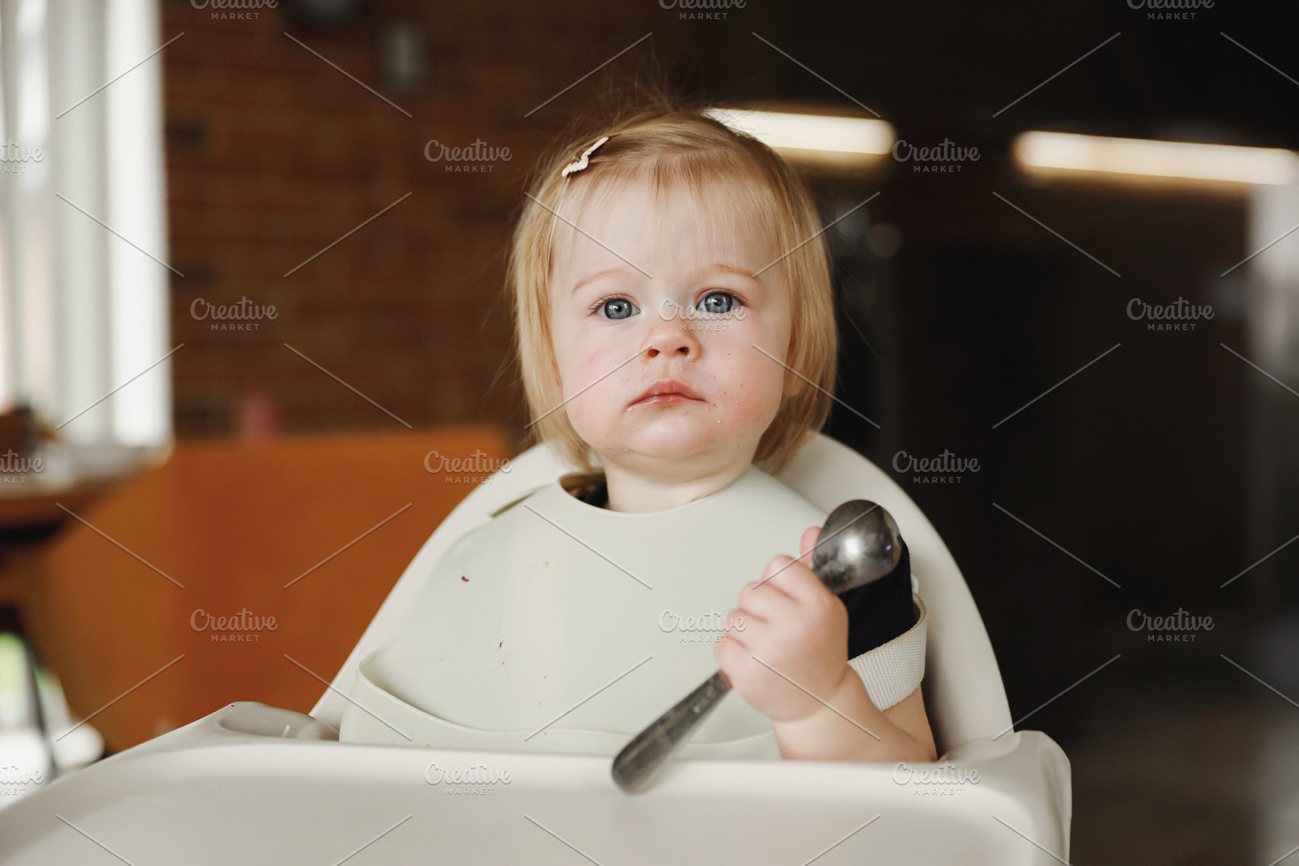 Infant girl or toddler sitting on high chair. Eating food by herself using spoo, a Person Photo by Lenor4ik