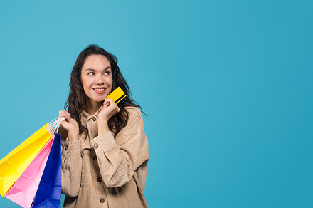 Glad millennial european brunette woman with bags shows credit card and looks a, a Background Photo by Prostock-Studio
