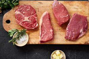 Raw rib-eye, roast beef, flank and rump steak displayed on a cutting board with