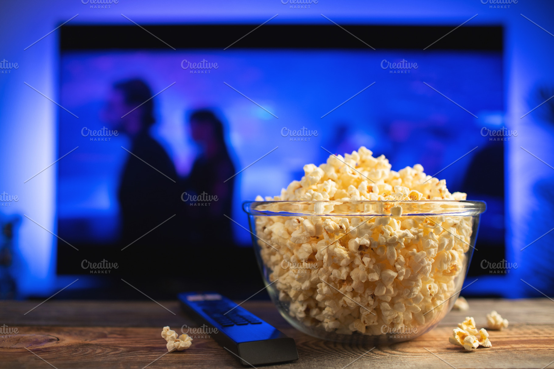 A glass bowl of popcorn and remote control in the background the TV works. Even, a Food & Drink Photo by Budarinphoto