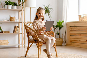 Girl with a tablet sitting on chair at living room while smiling, a Person Photo by DanFLCreativo