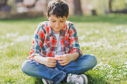 Smiling boy portrait sitting on city park grass while looking at camera, a Person Photo by RF Images
