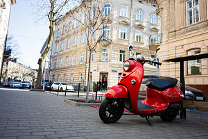 Red scooter parked on a street with classic European architecture, a Photo by AS photostudio
