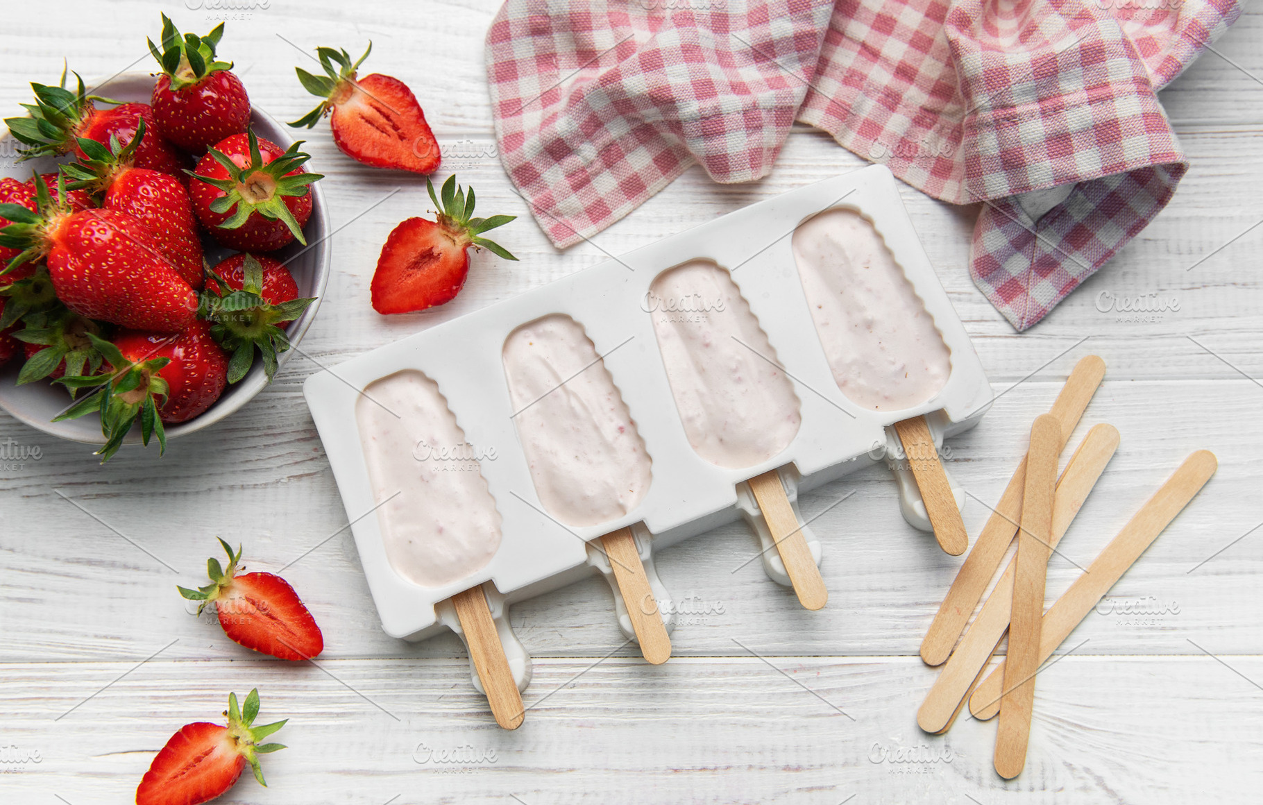 Strawberry popsicles in making process on white wooden surface, a Food & Drink Photo by Olena Rudo