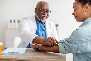 Black male doctor checking measuring pressure on patient's hand, a Photo by Prostock-Studio