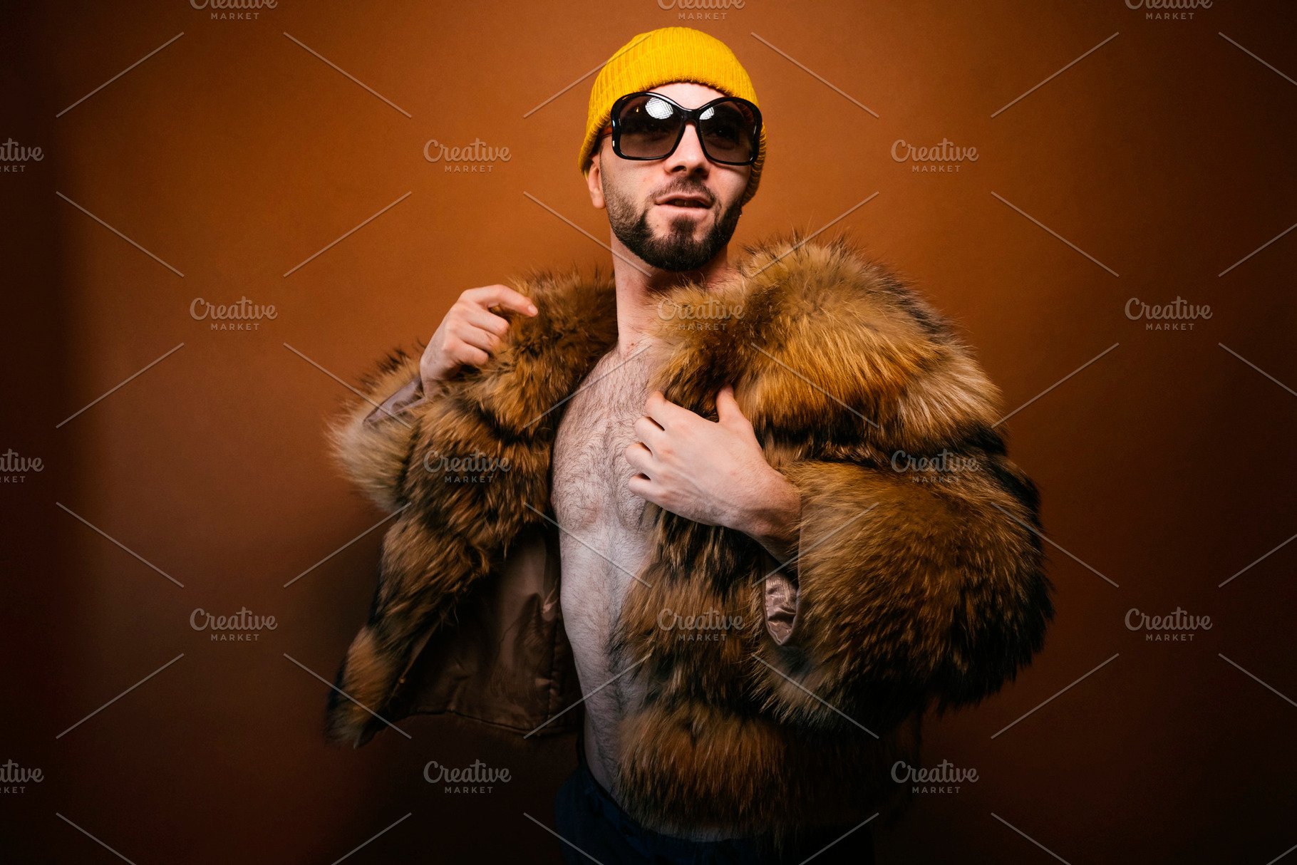 Man posing with furry jacket yellow beanie sunglasses, a Photo by karrastock