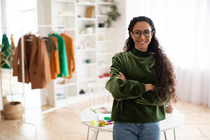 Cheerful Clothing Designer Woman Posing Near Clothing Rail Indoor, a Photo by Prostock-Studio