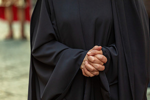 Close-up of a woman clasping her hands in prayer, wearing a black cassock durin, a Holiday Photo by Antonio Gravante Market