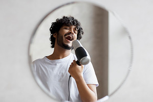 Joyful indian man having fun in the morning in bathroom, holding hairdryer and, a Person Photo by Prostock-Studio