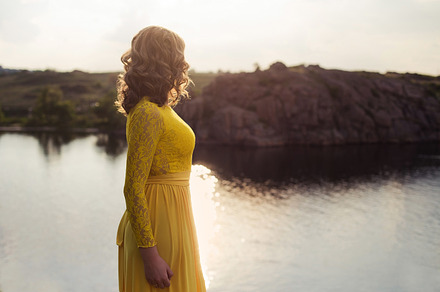 Young woman staying back. Attractive girl enjoys sunset near river and cliff in summer light, a Person Photo by Wedphoto