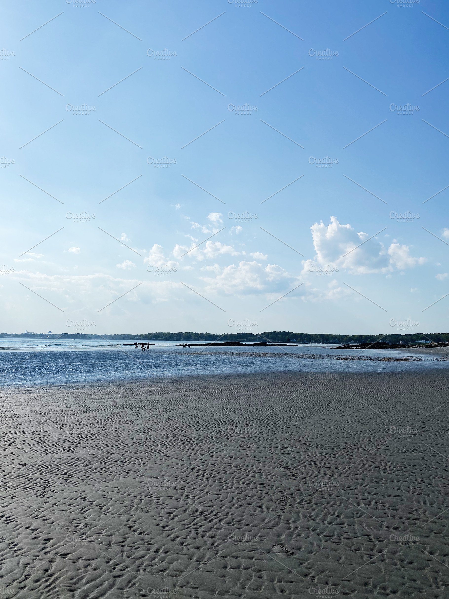 Sunny beach scene with calm water, rippled sand, and distant visitors, a Photo by AS photostudio