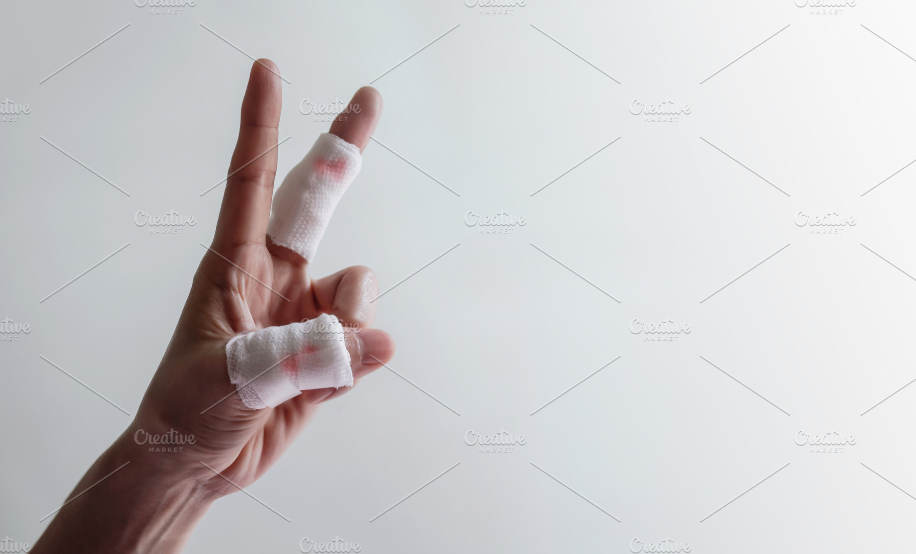 Hand with bandaged fingers raised against plain background. Conc, a Photo by salmon.black