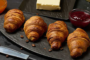 Golden croissants laid out in a row on a dark stone board, surro, a Food & Drink Photo by ndanko
