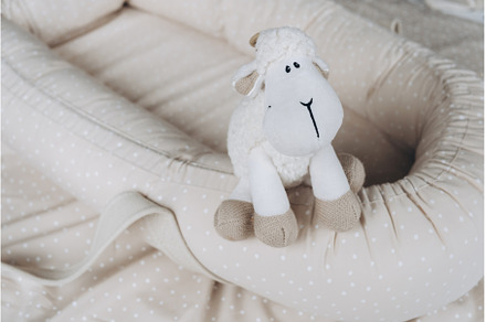 Soft sheep toy on beige cocoon, baby