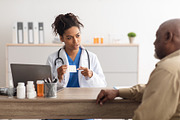 Female black doctor showing pills to male patient, a Photo by Prostock-Studio (Thumbnail 1 of 2)