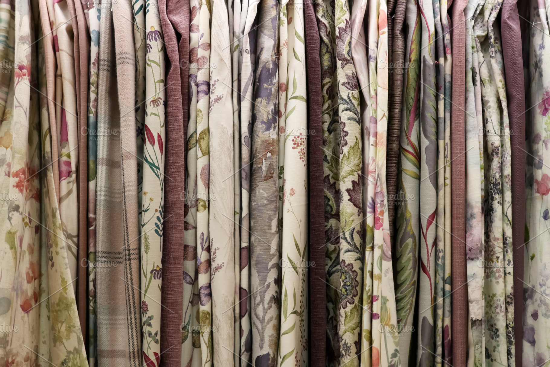 Diverse fabric samples hanging, displaying floral and nature inspired patterns, a Photo by Studio ANNA