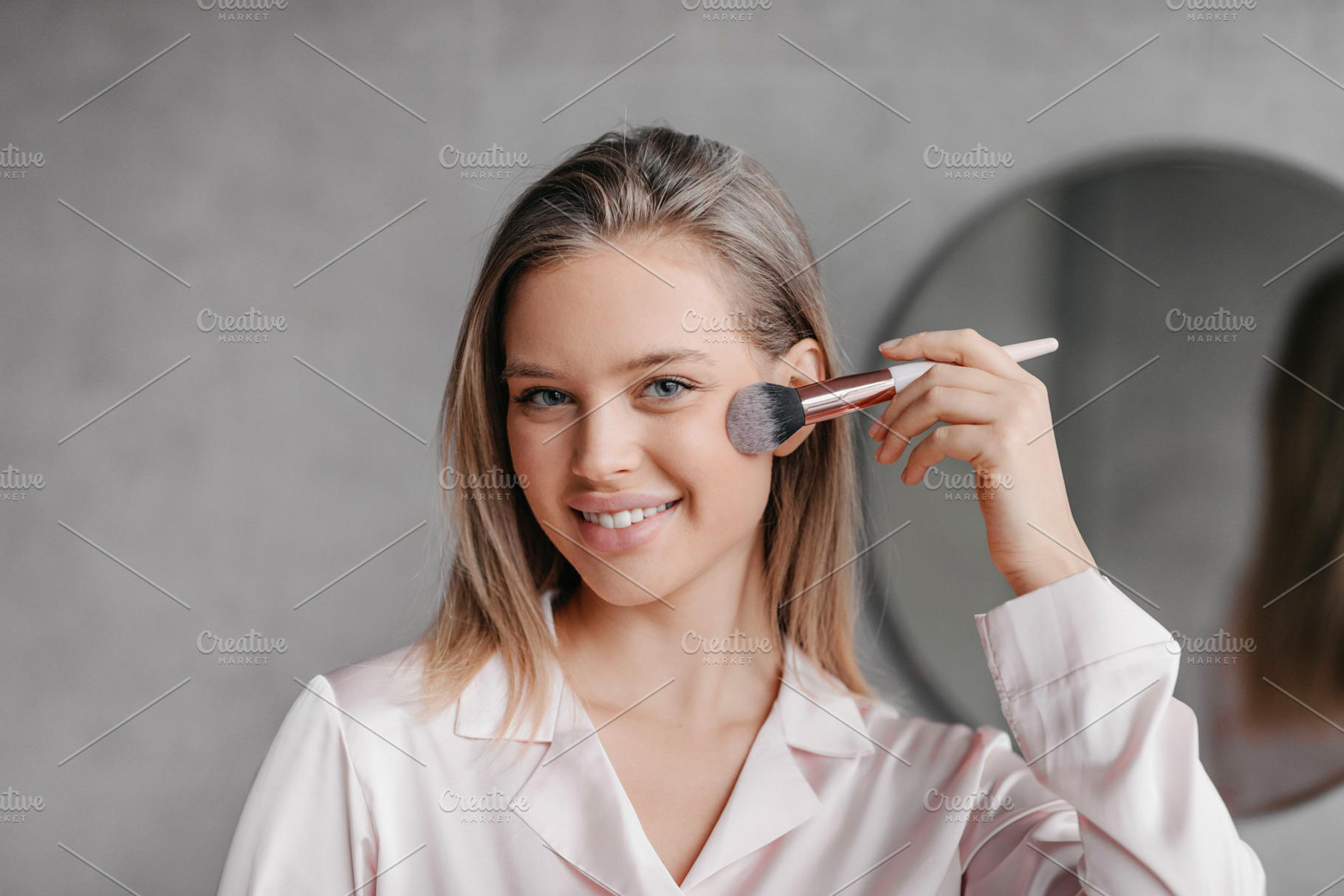 Young pretty lady doing makeup before going out, applying highlighter or blush, a Photo by Prostock-Studio