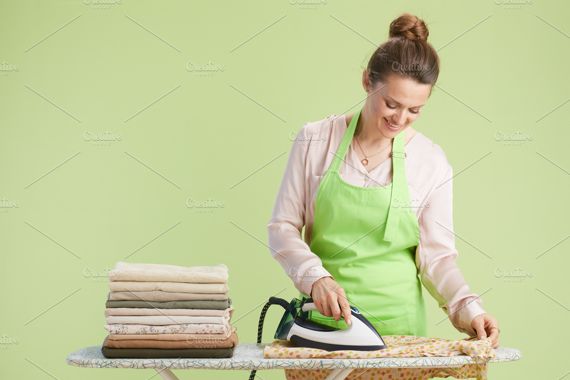 Woman ironing patterned fabric, pastel green backdrop, a Person Photo by Alliance Images