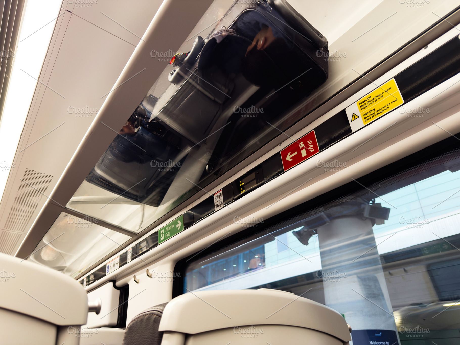 Travelers luggage stored overhead in modern train carriage with safety signs an, a Photo by AS photostudio