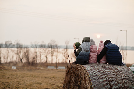 Back of four kids sitting on haycock at field against lake sunse, a Person Photo by AS photostudio