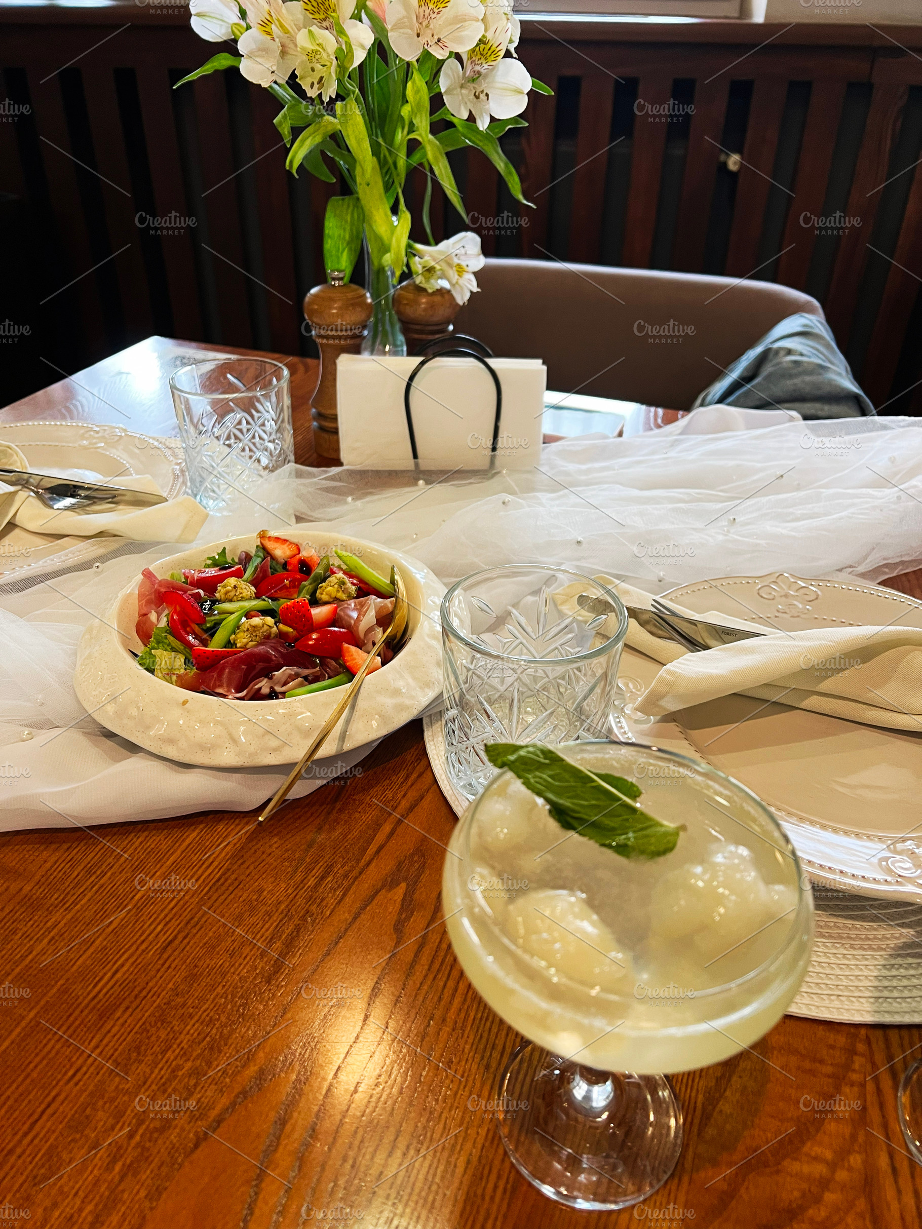 Elegant dining table with salad, cocktail, and decorative floral arrangement, a Photo by AS photostudio
