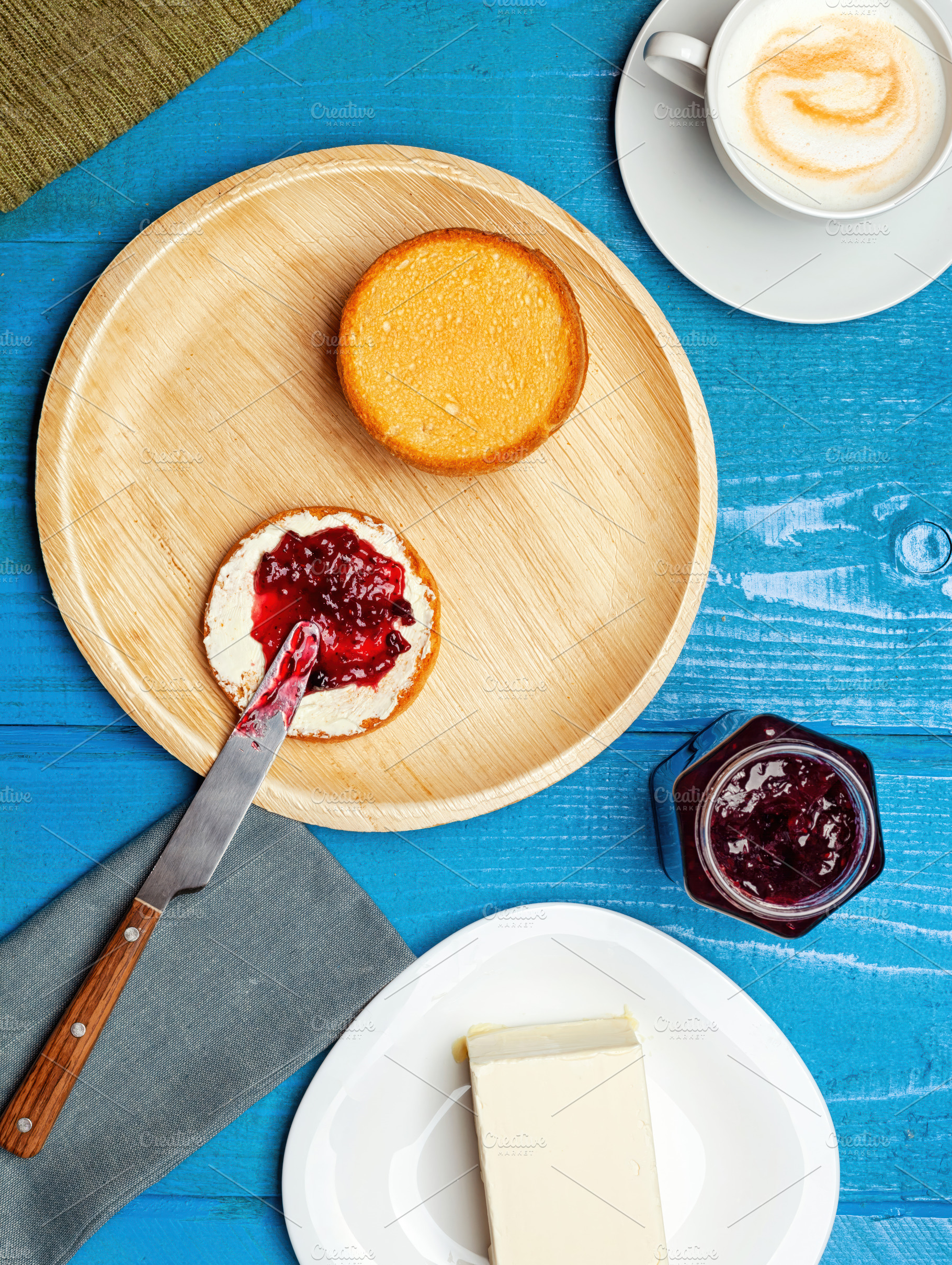 Preparing tasty breakfast with bread, butter, jam and cappuccino on blue wooden, a Food & Drink Photo by Antonio Gravante Market