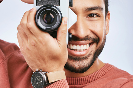 Happy man with camera, photography and smile in portrait with creativity and art isolated on studio background. Male photographer, creative with artistic person and taking pictures with gadget, a Photo by Peopleimages.com