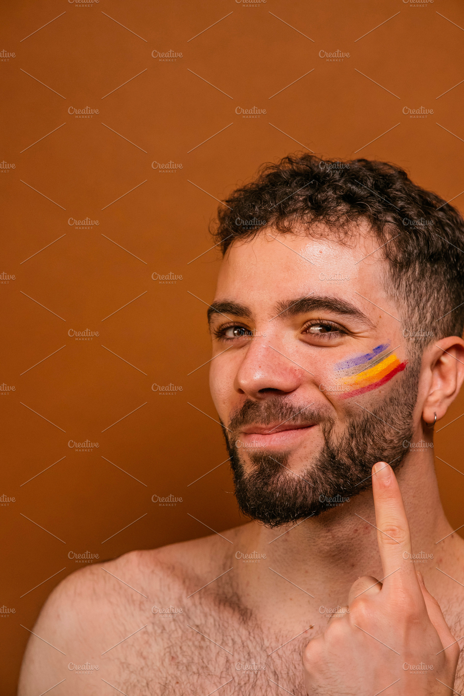 Young man smiling at camera with rainbow face paint, a Photo by karrastock