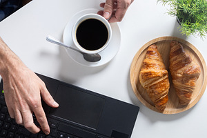 Remote Work Breakfast with Coffee and Croissants on Home Office Desk, a Food & Drink Photo by etorres69