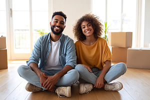 Young couple sits on floor of their new home surrounded by moving boxes and smi, a Photo by AlyaAnd