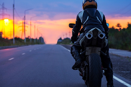 motorcyclist stands on an empty road at sunset , back view , cop
