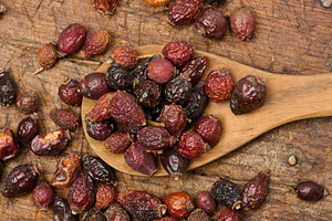 Dried rosehip fruits in a wooden spoon and on a table close-up., a Food & Drink Photo by ndanko
