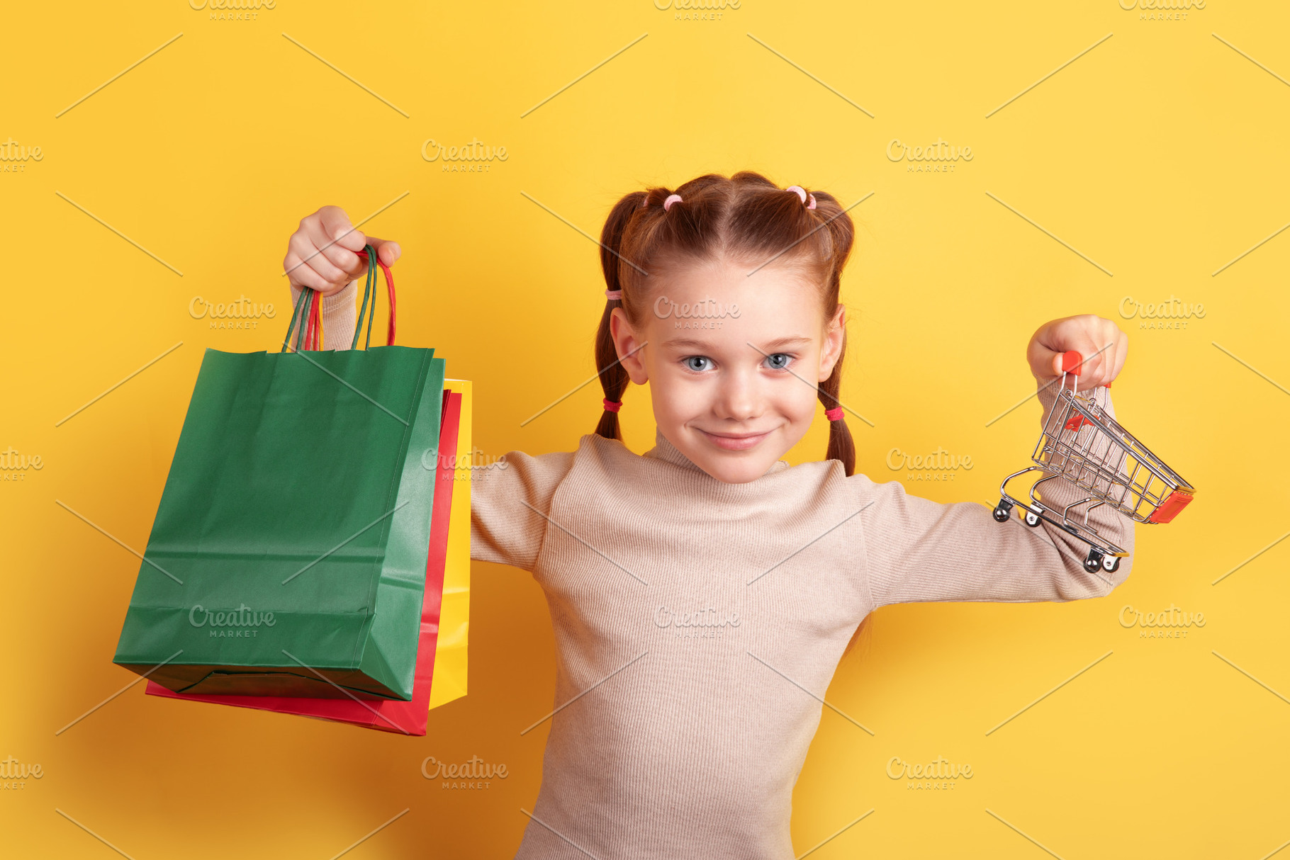 Smiling girl holding a shopping bag and miniature cart against a, a Person Photo by Ales Munt