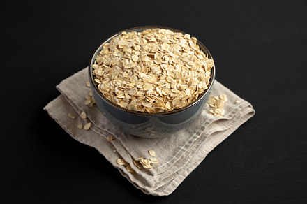 Wholegrain Oat Flakes in a Bowl on a black background, side view, a Food & Drink Photo by LiudmylaChuhunova