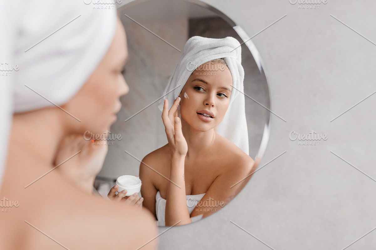 Home beauty routine. Young woman applying moisturising cream on face looking at, a Photo by Prostock-Studio (Photo 3 of 5)