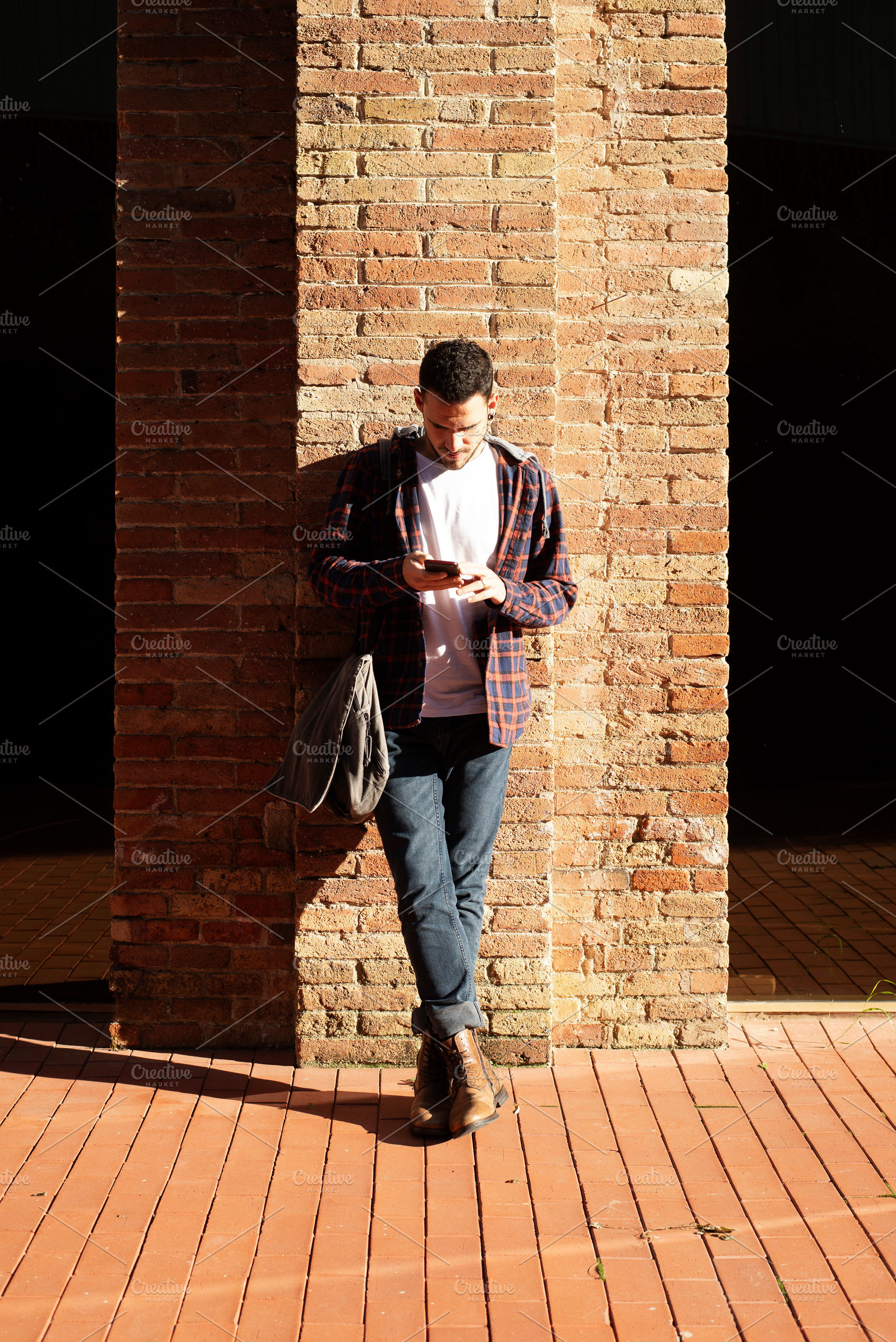 Young caucasian man using smartphone against brick wall, a Person Photo by RF Images