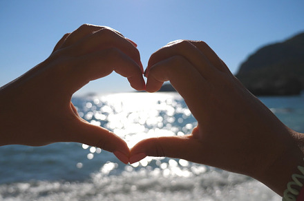 Young girl making heart shape with her hands over sea background on a sunny day. Summer holidays on the beach. Concept of vacation. Close up