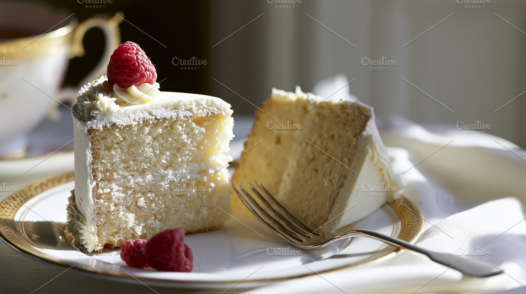 Vanilla cake slices with frosting and fresh raspberries on a golden rimmed plat, a Photo by Studio ANNA