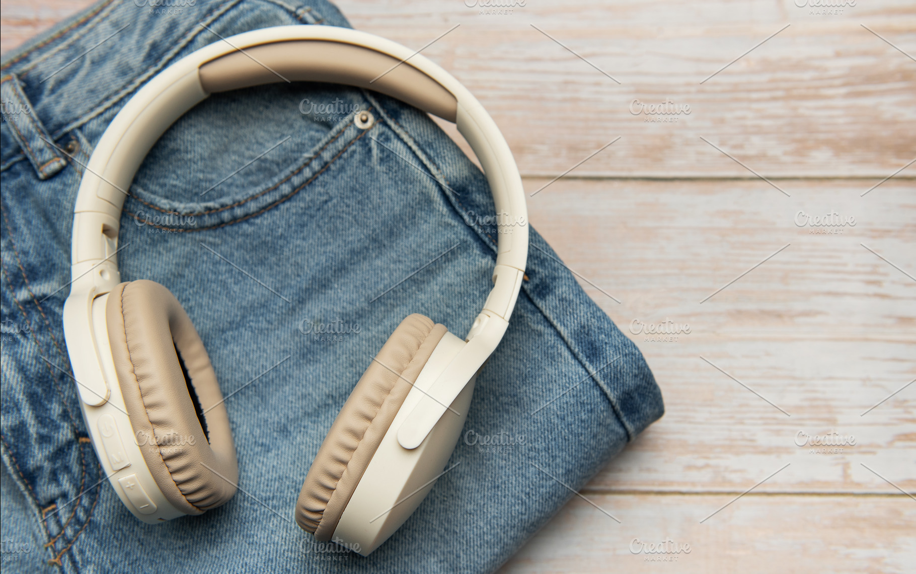 Wireless headphones lying on folded jeans on wooden table, a Technology Photo by Olena Rudo