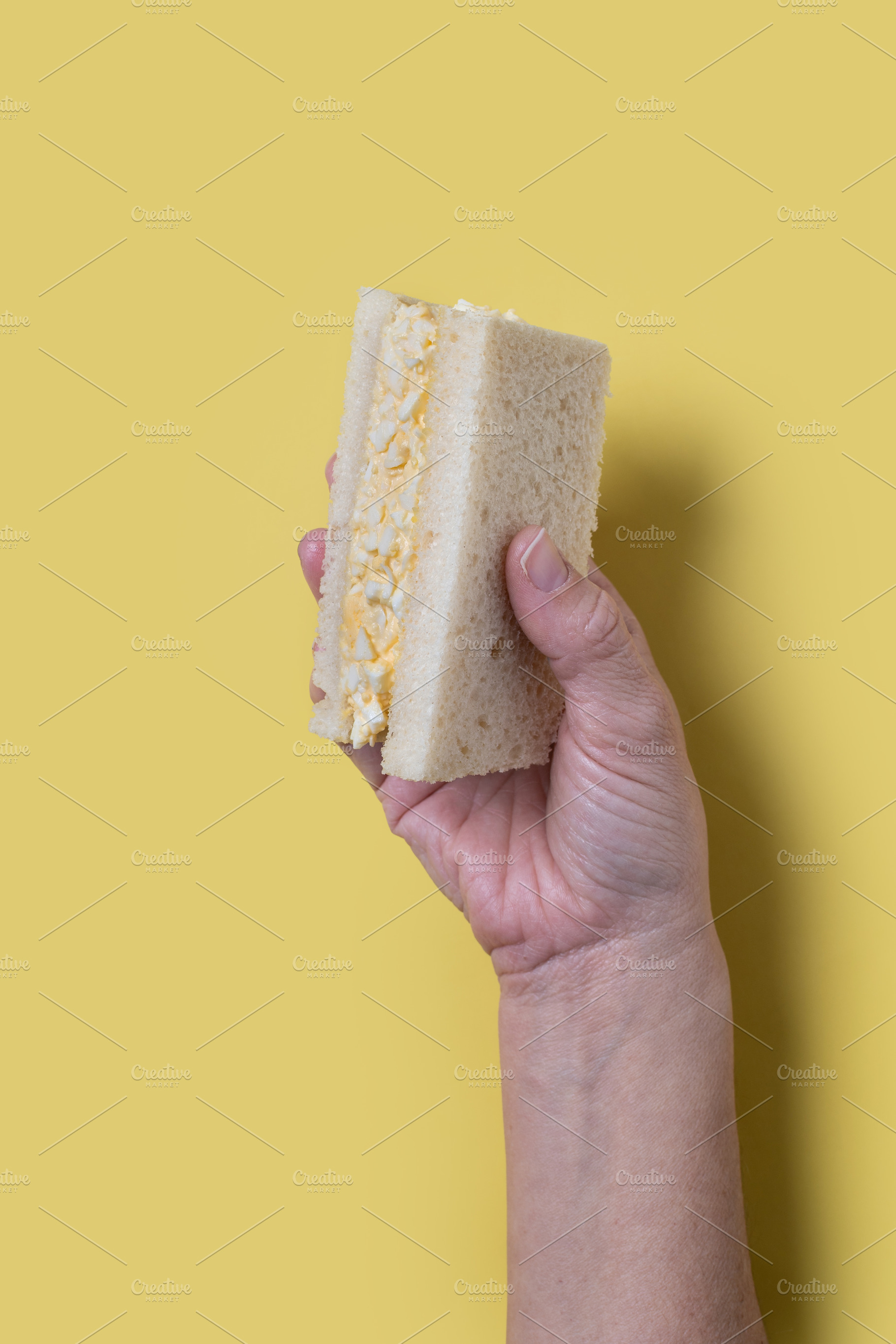 Hand holding a tamago Sando sandwich, a Photo by etorres69